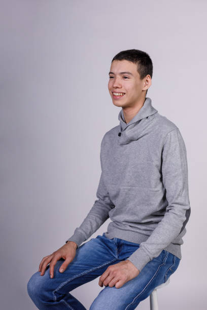 istock Charming teenage boy sitting against white background, smiling confidently 2150611761