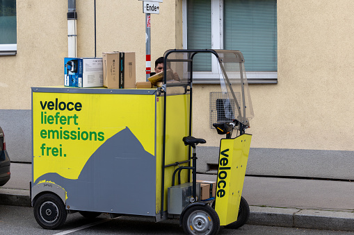 Vienna, Austria April 5, 2024 A postal delivery worker unloads packages from  an electric delivery vehicle and sign in German saying emissions free.
