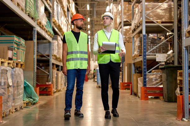 istock two engineers in helmets walking among shelves with goods in warehouse talking, checking 2150616039
