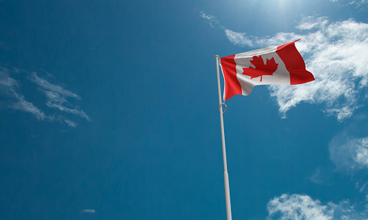 Canadian flag waving in the wind against the blue sky