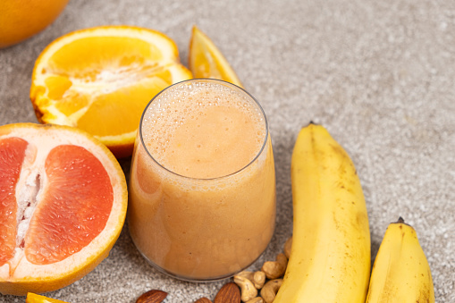 Fruit smoothie in a glass with banana, grapefruit and orange on grey background