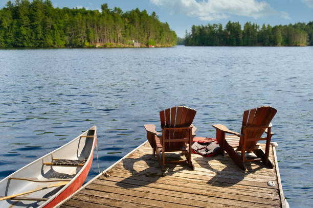 istock Two cottage Adirondack chairs on a dock overlook the lake. 2150628403