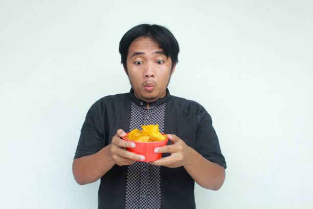 istock A young asian man with a surprised expression holds a bowl of potato snacks. 2150633985