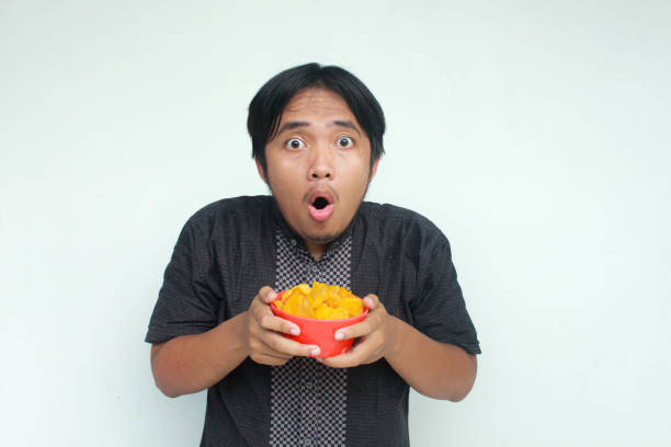 istock A young asian man with a surprised expression holds a bowl of potato snacks. 2150634018