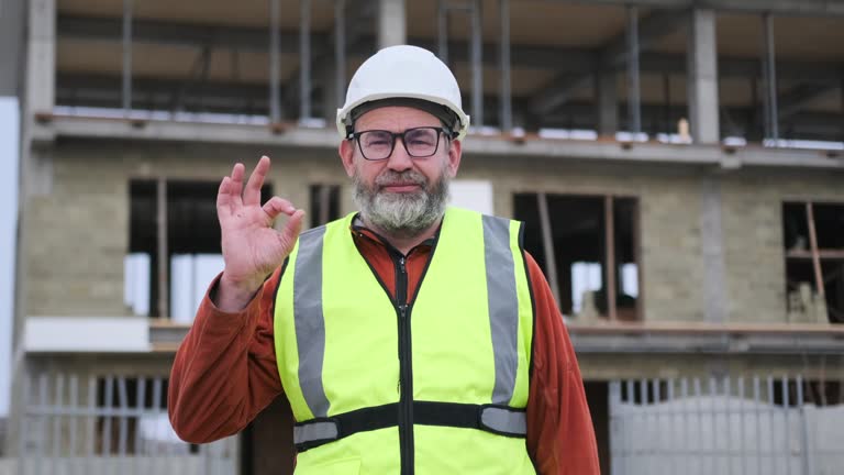 Bearded male civil engineer showing ok gesture with thumbs up at construction site