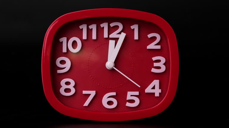 Close-up of red clock time lapse on black background. The hands of the red wall clock move back quickly.
