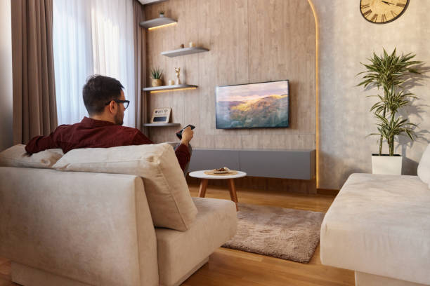 Back view of a man watching TV at home.