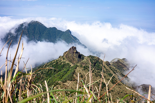 View of the ridge of Teapot mountain with blurred grass in the foreground. White clouds drift like mist between the mountain peaks.