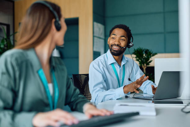 istock Black businessman communicating with coworker while working on laptop in the office. 2150644309