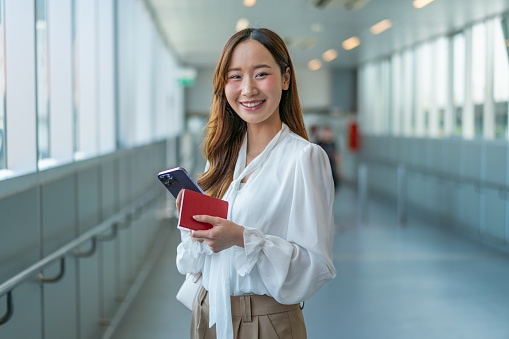 Modern Asian Woman Smiles, Holding Passport and Phone, En Route to the Airport