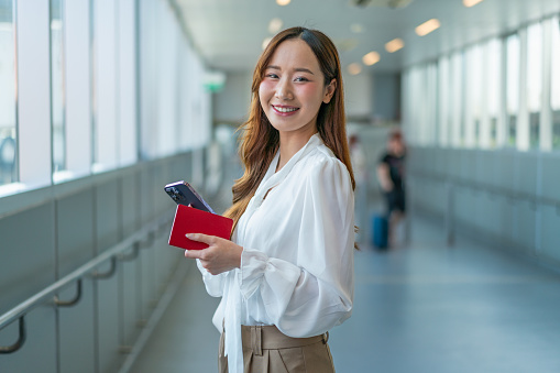 Modern Asian Woman Smiles, Holding Passport and Phone, En Route to the Airport