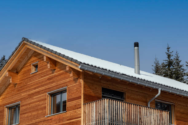 Wooden house with stainless steel chimney and thin blanket of snow on the roof