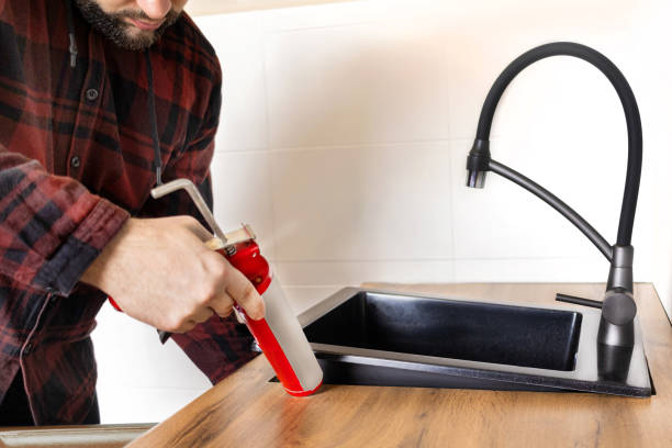 istock A man installs a black stone sink into a kitchen countertop. Worker seals up the kitchen sink with a sealant using a construction sealing gun 2150650218