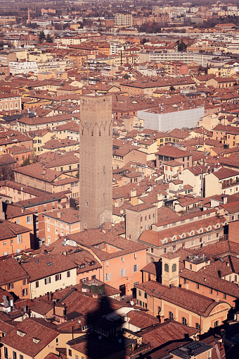An aerial view of central Bologna, Italy, featuring a medieval tower among densely packed buildings with terracotta roofs. Vertical photo has a warm, vintage look