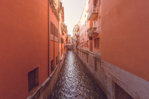 A hidden gem, the Canale delle Moline in Bologna, is framed by terracotta-hued buildings in a photo that exudes a vintage charm