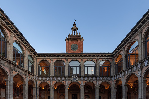 Golden hour light gently kisses the terracotta facade of the University of Bologna, framing the historical main entrance and its clock tower, a portal to centuries of academic excellence