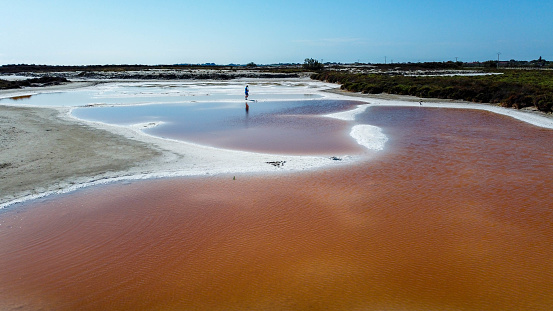 man walking barefoot in a salt strip surrounded by salty pink water. tourist point in Provence in the Camargue Regional Natural Park where the salin de giraud are located. Stage of a trip to France in the midst of nature. tranquility and carefreeness on a summer holiday in France.