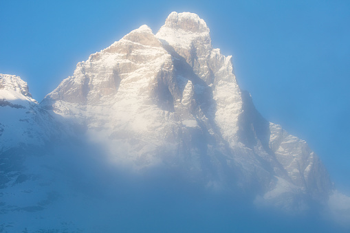 The sun is so low on the horizon, at dusk, that its rays light up only the highest peaks, among them the mighty Matterhorn, shrouded in mist, here seen from the Italian side.