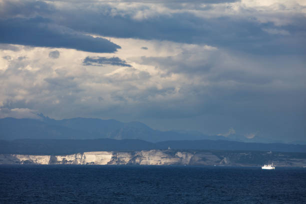 From the head of Cape Testa, the incoming storm from the Strait of the Straits of Bonifacio is evident. Across the strait, the white cliffs of Bonifacio are still illuminated by the sun's rays, rather dramatically.