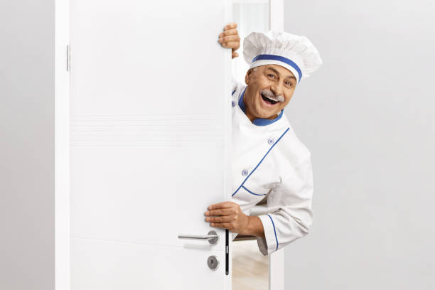 istock Mature male chef in a uniform opening a door 2150656088