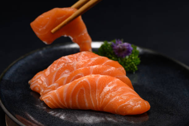 istock Chopsticks with sliced raw salmon over black background. Close up shot 2150656272