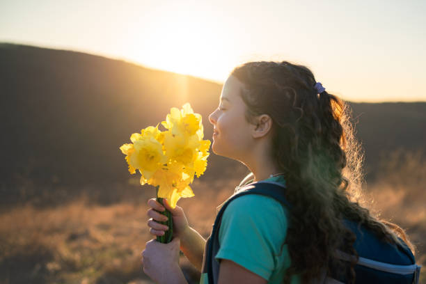 A beautiful child holding a yellow flower in her hand on the road.