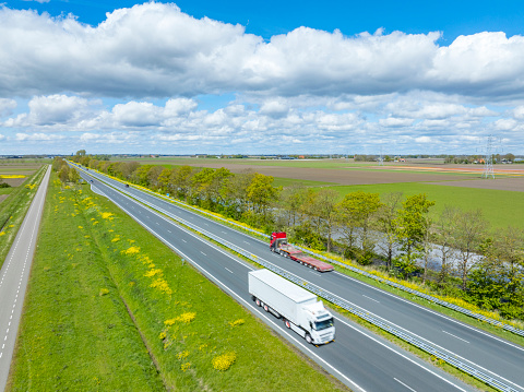 Cars and Trucks with freight cargo trailers driving on the N50 road near Ens and Emmeloord in the Noordoostpolder in Flevoland, The Netherlands. High angle drone image with motion blur.