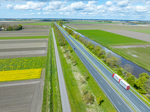 Cars and Trucks with freight cargo trailers driving on the N50 road near Ens and Emmeloord in the Noordoostpolder in Flevoland, The Netherlands. High angle drone image with motion blur.