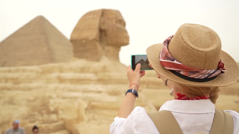 4K Video of Woman standing in front of the background of Giza pyramids and Sphinx and taking pictures with smartphone. Giza, Cairo, Egypt