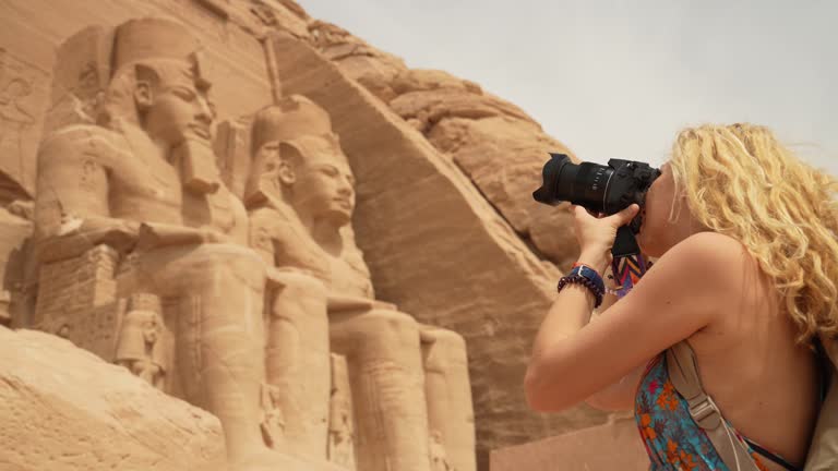 4k Video of Female photographer in vacation standing with photo camera in front of the incredible Abu Simbel Temple rebuilt on the mountain in southern Egypt in Nubia next to Lake Nasser. Temple of Pharaoh Ramses II. Egypt, Aswan, Abu Simbel