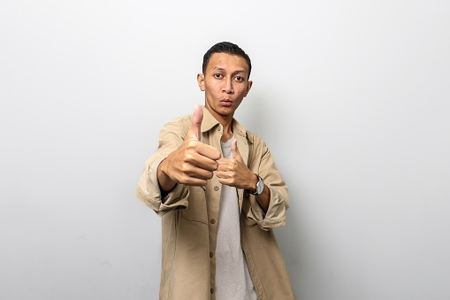 Asian man in tan jacket with like or thumb up hand gesture showing his best