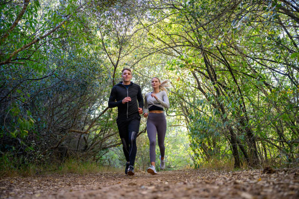 istock Front view young couple running together on footpath through forest 2150660464