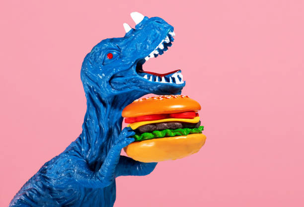 istock Close up blue dinosaur holding burger on pink background. 2150663814
