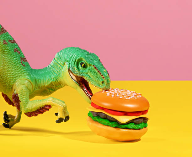 istock Green dinosaur bites a burger on pink and yellow background. 2150663837