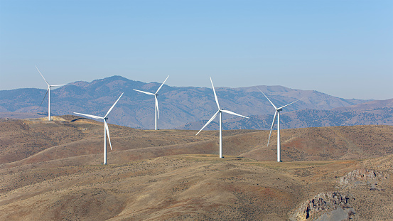 Aerial view of wind turbines spinning on mountain tops against sky on sunny day in Oregon, USA.