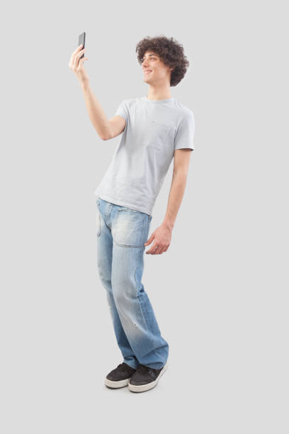 istock Young happy smiling handsome man using his smartphone, taking a selfie isolated against a gray background, full body image 2150665541