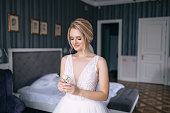 A luxurious bride in a white dress with a veil on her head holds a boutonniere in her hands.