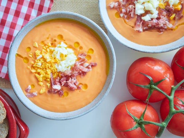 istock Spanish cold tomato soup called salmorejo. Served in bowls, with chopped hard-boiled egg, diced Serrano ham and olive oil. Fresh red tomatoes on the table. Close-up view from above. 2150665843