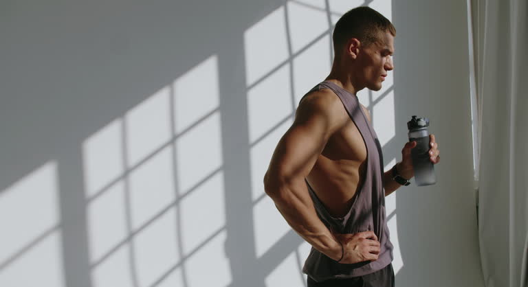 Athletic 23-Year-Old Man Drinking Water After Training in Studio