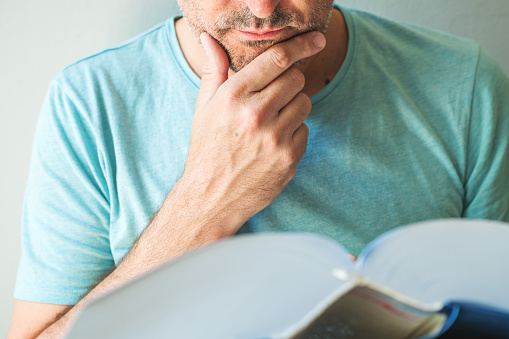 Closeup of male reading book and stroking chin, selective focus