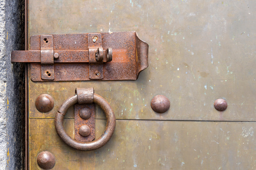 Copper door with rivets, a rusty bolt and a knocker handle. Metal structure is visible.
