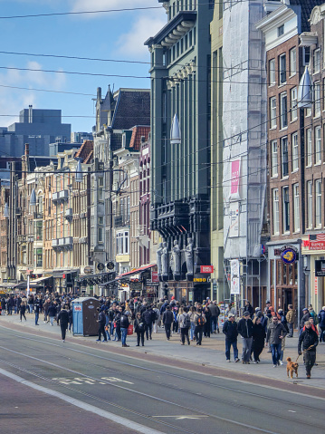 Amsterdam Netherlands 21 April 2024 A diverse group of people walks in a lively hustle down a bustling city street flanked by shops, under a clear blue sky.