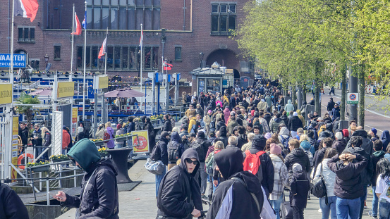 Amsterdam Netherlands 21 April 2024, A vibrant scene unfolds as a large group of diverse individuals leisurely stroll down a bustling city street, creating a dynamic flow of movement and energy.