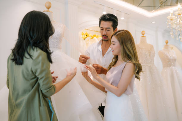 istock Asian bride is smiling while choosing wedding dress in modern wedding salon. 2150674006