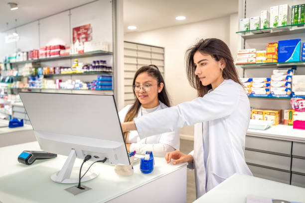 two pharmacist using computer at counter - farmácia imagens e fotografias de stock
