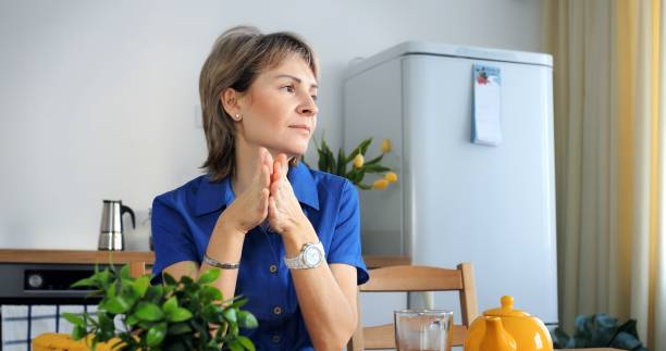 istock Pensive woman procrastinates at kitchen table, distant gaze. Conceptual procrastination, tea untouched, decision delayed. Procrastination theme, cinematic home setting, trendy lifestyle portrayal. 2150676212