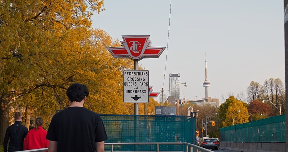 Toronto, Canada - May 6, 2023: Urban stroll in Toronto, autumn mood, bustling cityscape. Vibrant street life beneath CN Tower, iconic Canadian landmark in view. Pedestrian sign directs, urban scene