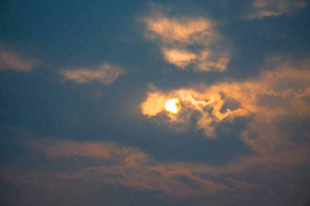 The sky is cloudy and the sun is shining through the clouds. The sun is a bright yellow color and it is shining through the clouds