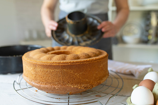 Fresh baked bundt cake on a cooling grid with woman in the background with empty baking pan in the kitchen