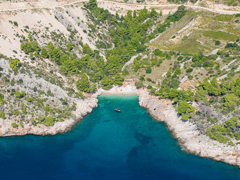 AERIAL: Scenic drone shot of a hidden gem of a sandy beach with turquoise water and a small group of tourists enjoying their summer vacation in Croatia. Relaxed tourists having fun at a secluded beach
